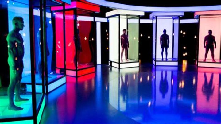 Six naked men stand in dimly lit, neon-colored boxes.